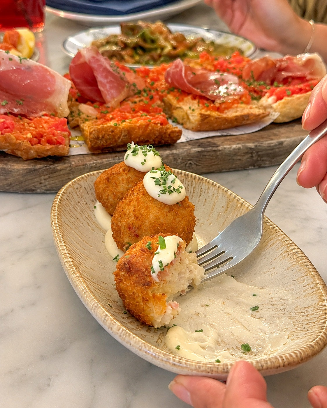 Hands sharing croquetas and tapas at Pikoteo